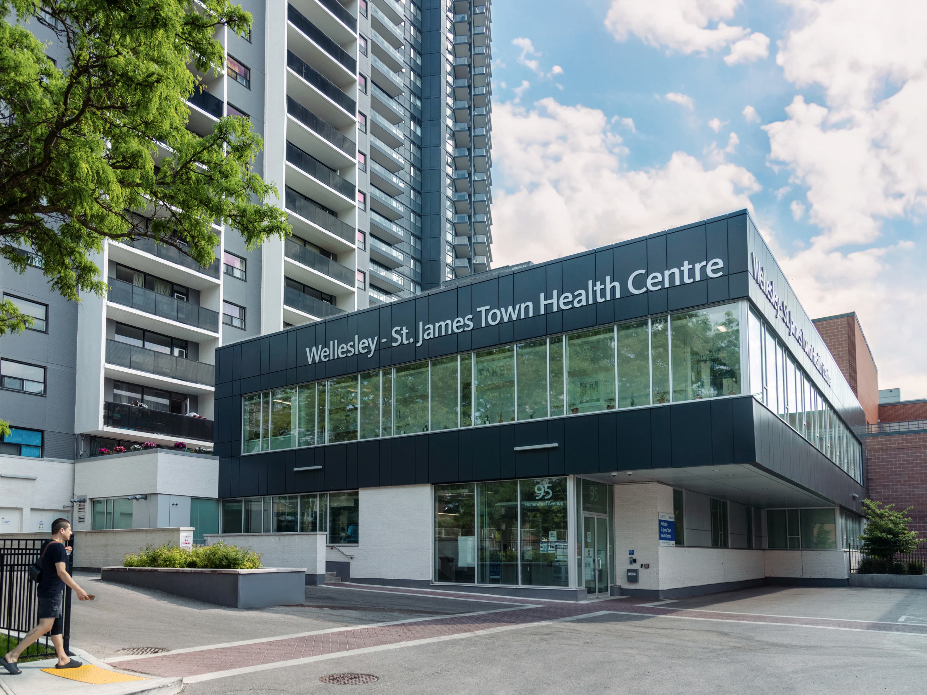 At 155 Wellesley, the Wellesley–St. James Town Health Centre occupies a two-storey L-shaped podium that wraps the base of the residential tower. This form binds the tower to the street and emphasizes its civic role, with dark metal cladding and generous glazing creating a clear public identity. The transparent second level connects the centre to the surrounding neighbourhood, while the ground floor provides accessible community-focused services. Together, the podium and tower integrate housing and healthcare within a unified urban presence.