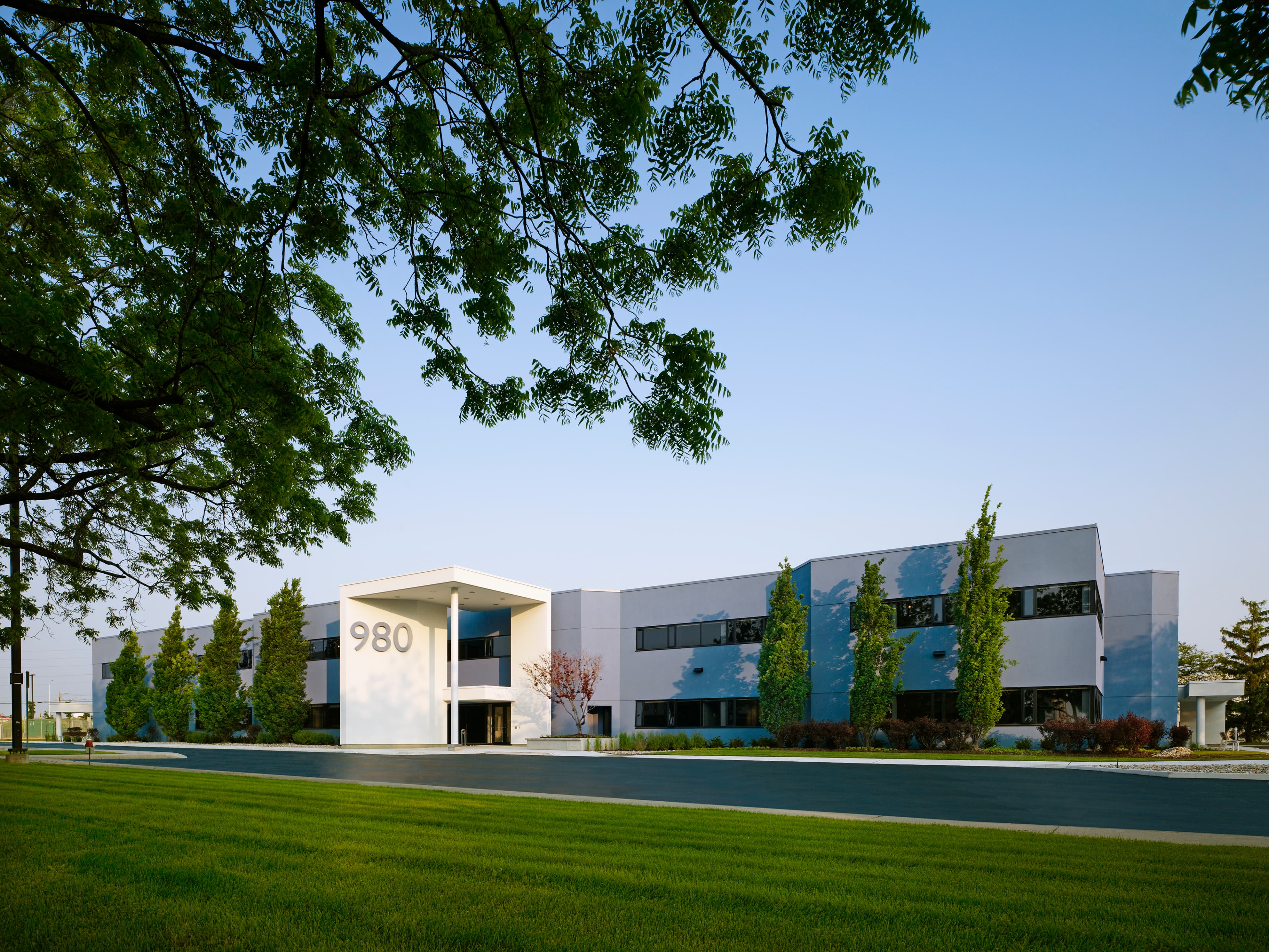 A 1970s single-tenant commercial building was converted into a 5,000 m² multi-tenant office complex. The redesign introduced a central entry with a canopy and drop-off, a new rear entrance from the main parking lot, and updated systems throughout. New windows and a blue stucco façade with white canopies and dark-framed glazing give the building a stronger identity, while mature landscaping was carefully preserved.
