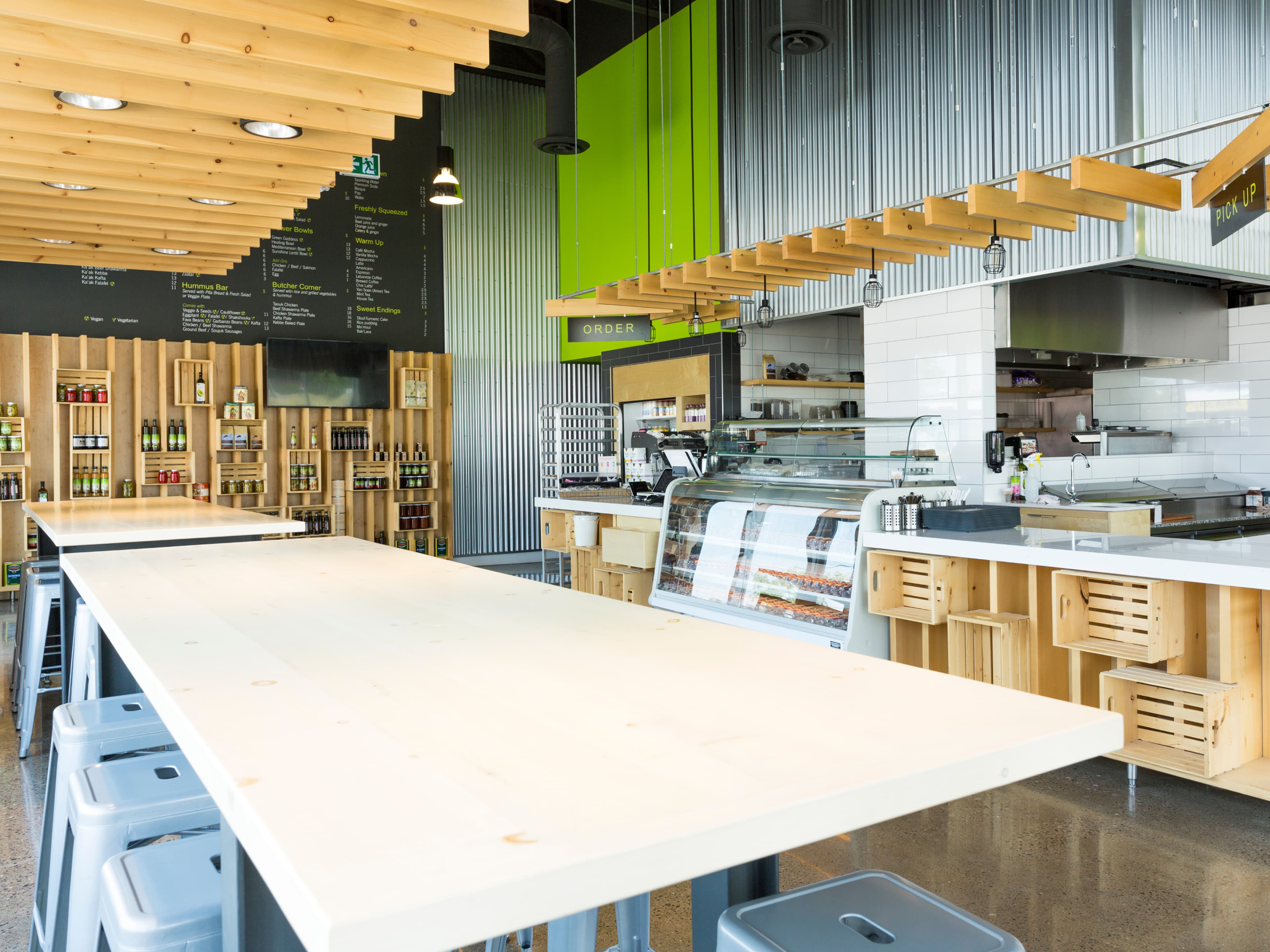 A fast-casual Mediterranean restaurant designed to pair efficiency with warmth. The layout places open kitchen and service counters at the center, framed by communal tables and shelving that doubles as display for pantry goods. Materials such as corrugated steel, polished concrete, bright accent colors, and simple wood elements create an atmosphere that feels both industrial and inviting, highlighting the fresh, everyday quality of the food.